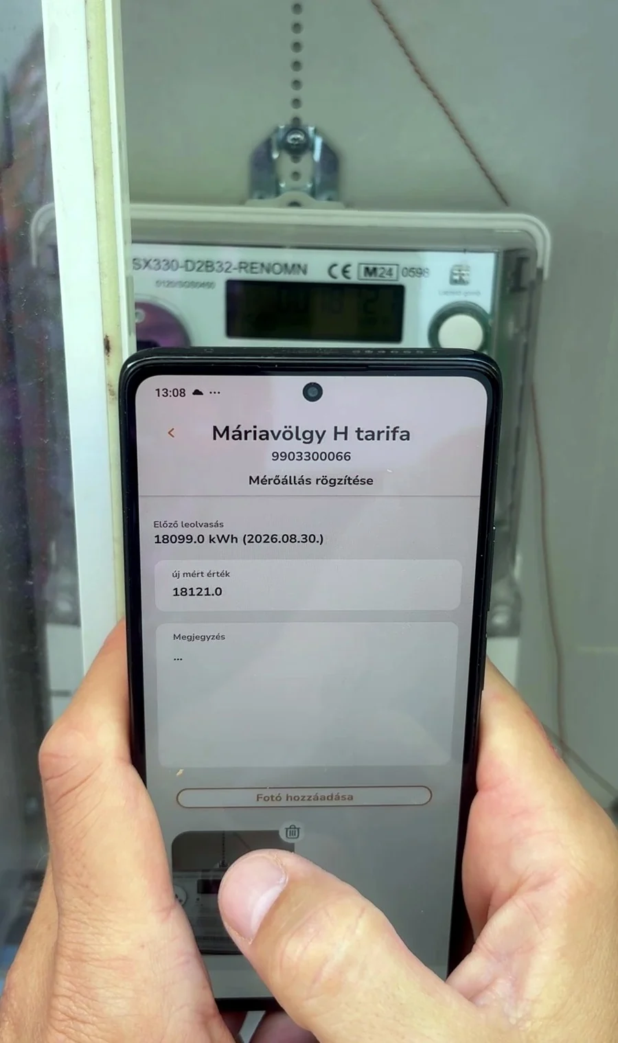 Kéz telefonnal egy valódi mérőóra-szekrény előtt; a képernyőn a rögzített mérőállás
