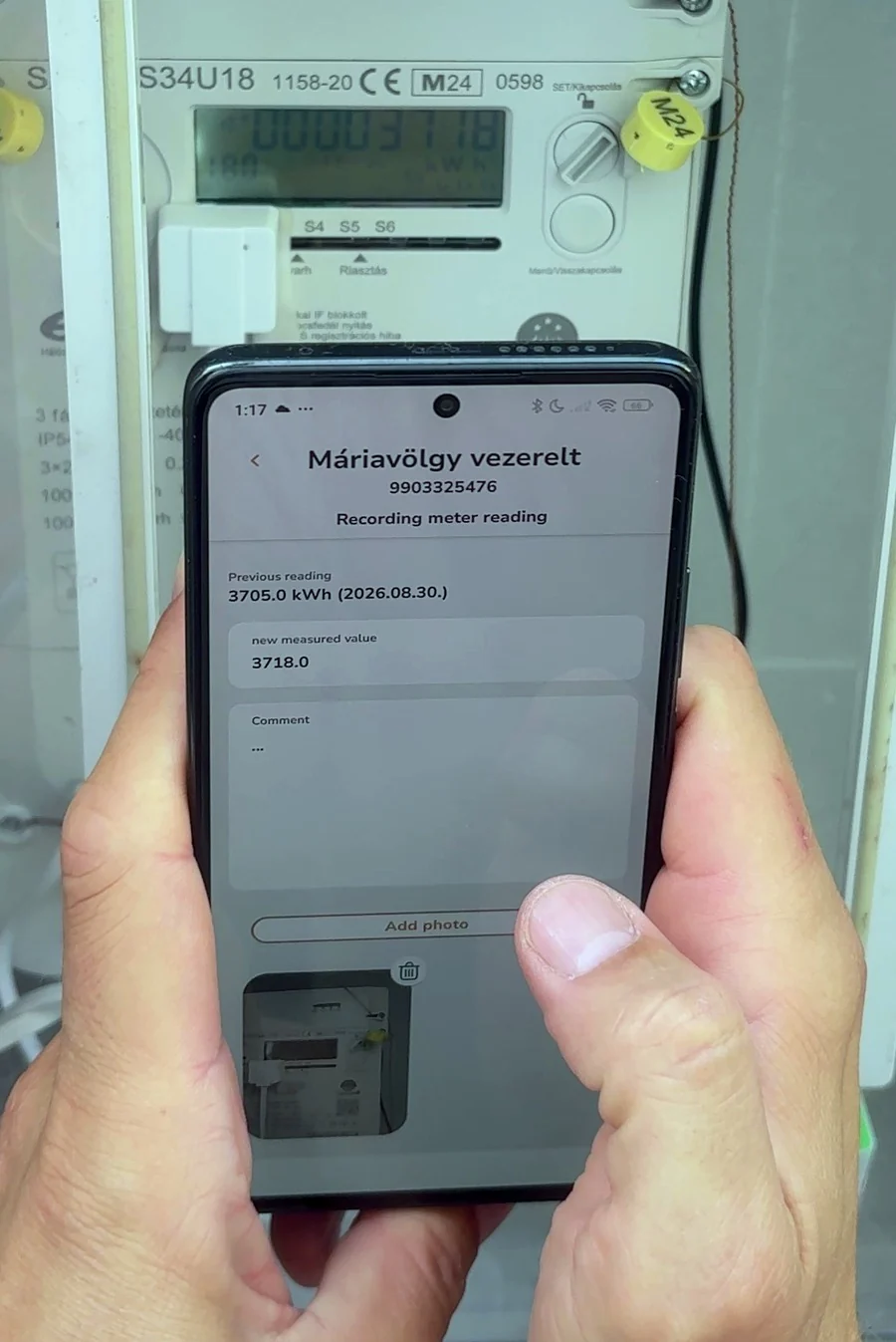 Hands holding a phone in front of a real electricity meter cabinet, the captured reading on screen